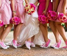 a group of women standing next to each other in pink dresses and converses holding bouquets