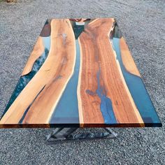 a table made out of wood and glass on top of gravel road next to water