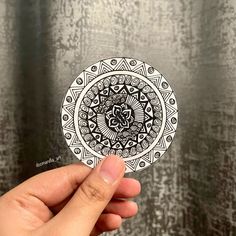 a hand holding up a sticker with an intricate design