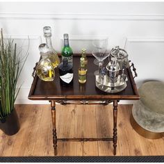 a table topped with bottles of wine and glasses next to a potted plant on top of a hard wood floor