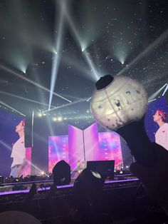 a person holding up a white ball in front of a stage with lights on it