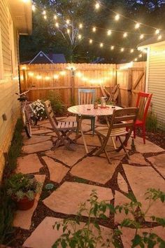 an outdoor patio with lights strung over it and chairs around the table, surrounded by greenery