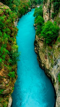 a river flowing through a lush green forest covered hillside next to tall rock formations on either side