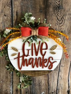 a wooden sign that says give thanks with fall foliage and red bow hanging on it