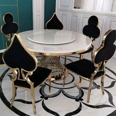 a white table with black chairs and gold trimmings on the top, in front of a blue wall