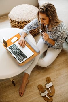 a woman is sitting on the floor with her laptop and sandal wedges in front of her