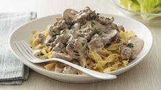 a white plate topped with pasta covered in meat and gravy next to a bowl of lettuce