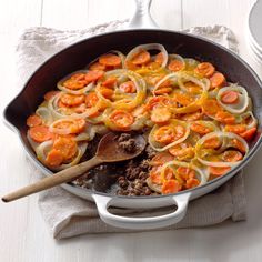 a skillet with onions, carrots and meat in it on a white table