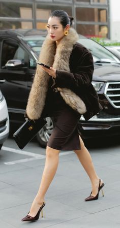 a woman walking down the street with a fur stole around her neck and heels on