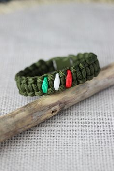 a green bracelet with red, white and green beads sitting on top of a piece of wood