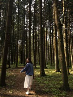 a woman standing in the middle of a forest with lots of trees on both sides