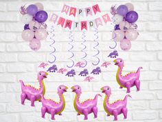 pink and purple dinosaur balloons are in front of a white brick wall