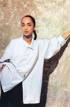 a woman standing in front of a wall with her hand on the side of her head