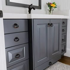 a bathroom with gray cabinets and a white sink in front of a mirror on the wall