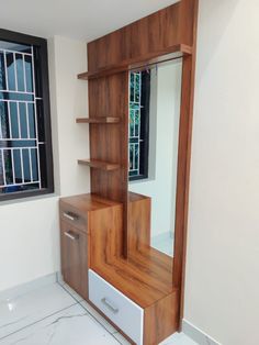 an empty room with a mirror and wooden shelf in the corner, next to a window