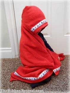 a child wrapped in a red towel sitting on the floor next to a white door