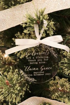 a glass ornament hanging from the top of a christmas tree with white ribbon