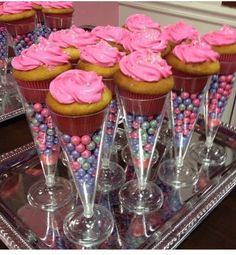 cupcakes with pink frosting and candy on a glass tray in front of other cupcakes