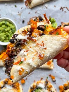 a hand holding a tortilla filled with black beans, cheese and cilantro