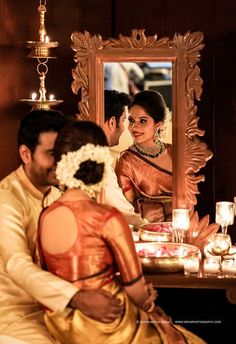 a man and woman sitting in front of a mirror with candles on the table behind them