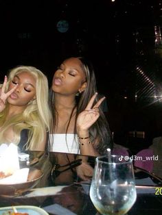 two women sitting at a table with food and drinks in front of them, making the peace sign