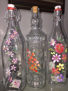 three glass bottles with flowers painted on them