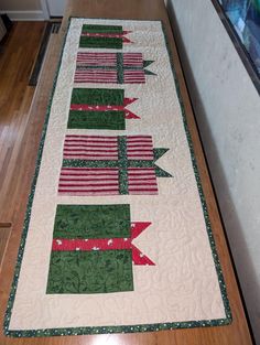 a quilted table runner with red and green ribbons on it's edges, sitting on a wood floor