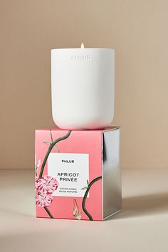 a candle sitting on top of a pink box next to a white container with flowers