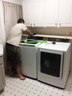 a man that is standing next to a washer and dryer in a kitchen