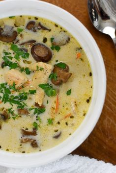 a white bowl filled with soup sitting on top of a wooden table next to a spoon