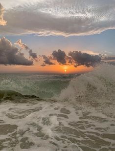 the sun is setting over the ocean with waves crashing in front of it and dark clouds