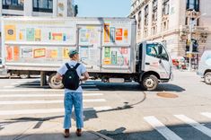 a man is walking across the street in front of a truck with advertisements on it