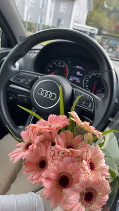 pink flowers in a vase sitting on the dashboard of a car with steering wheel controls