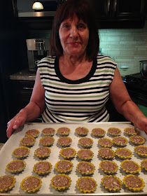 a woman is holding a tray full of hamburger patties on a counter in the kitchen