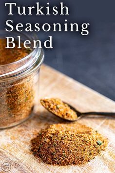 a wooden cutting board topped with a jar filled with seasoning next to a spoon