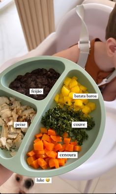 a baby in a highchair holding a tray with different foods on it, including carrots, celery, and beans