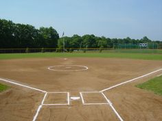 an empty baseball field with white lines painted on the dirt and trees in the background