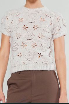 a woman in brown pants and a white top with crocheted flowers on it