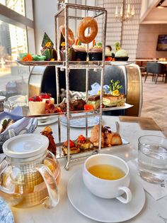 a table topped with plates and cups filled with food next to a tea pot full of donuts