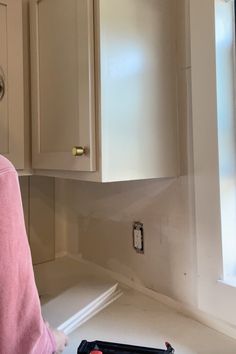 a woman standing in front of a kitchen counter top with tools on the counter and cupboards behind her