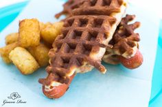 a waffle sandwich and some tater tots are on a blue paper plate