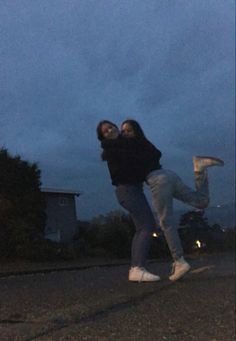 two people are jumping in the air on a street at night with their arms around each other