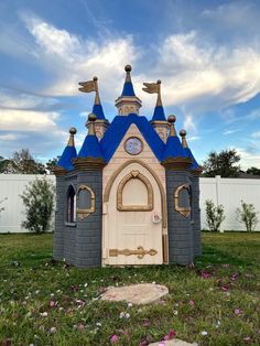 a small castle like structure with blue roof and two towers on the top, sitting in grass