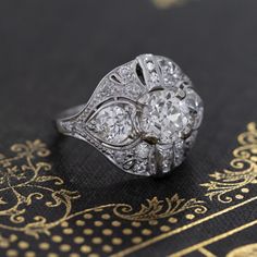 an antique diamond ring sits on top of a black and gold book with ornate designs