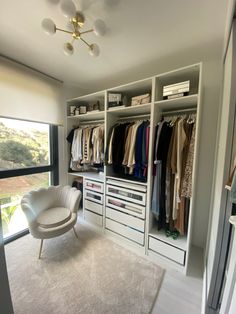 a room with a chair and some clothes on the closet shelves in front of a large window