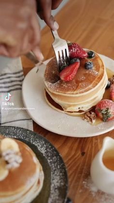 a person is cutting into some pancakes with fruit on top