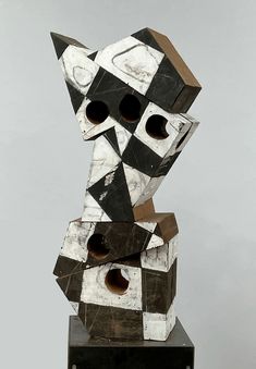 a black and white sculpture sitting on top of a wooden block with holes in it