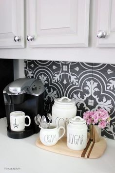 a kitchen counter with coffee maker, mugs and pink flowers on the counter top