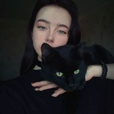 a woman holding a black cat up to her face and looking at the camera with green eyes