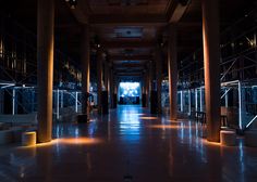 the inside of a building with columns and lights on each side of the room, all lit up at night